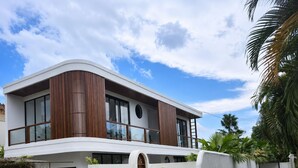 Une maison moderne à deux étages, dotée d’un toit incurvé, de grandes fenêtres et d’une façade blanche.