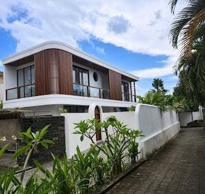 Une maison moderne à deux étages, dotée d’un toit incurvé, de grandes fenêtres et d’une façade blanche.