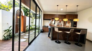 Une cuisine moderne dotée d’un îlot central, de tabourets de bar et d’une porte vitrée donnant sur un jardin.