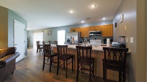 A modern kitchen with wooden cabinets, a stainless steel refrigerator, and a built-in microwave. There are four wooden bar stools and a dining table with chairs. - Quiet, Family Friendly 3/2 Home (Columbia)