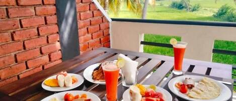 A table with breakfast items and a drink, set against a brick wall and a view of greenery.
