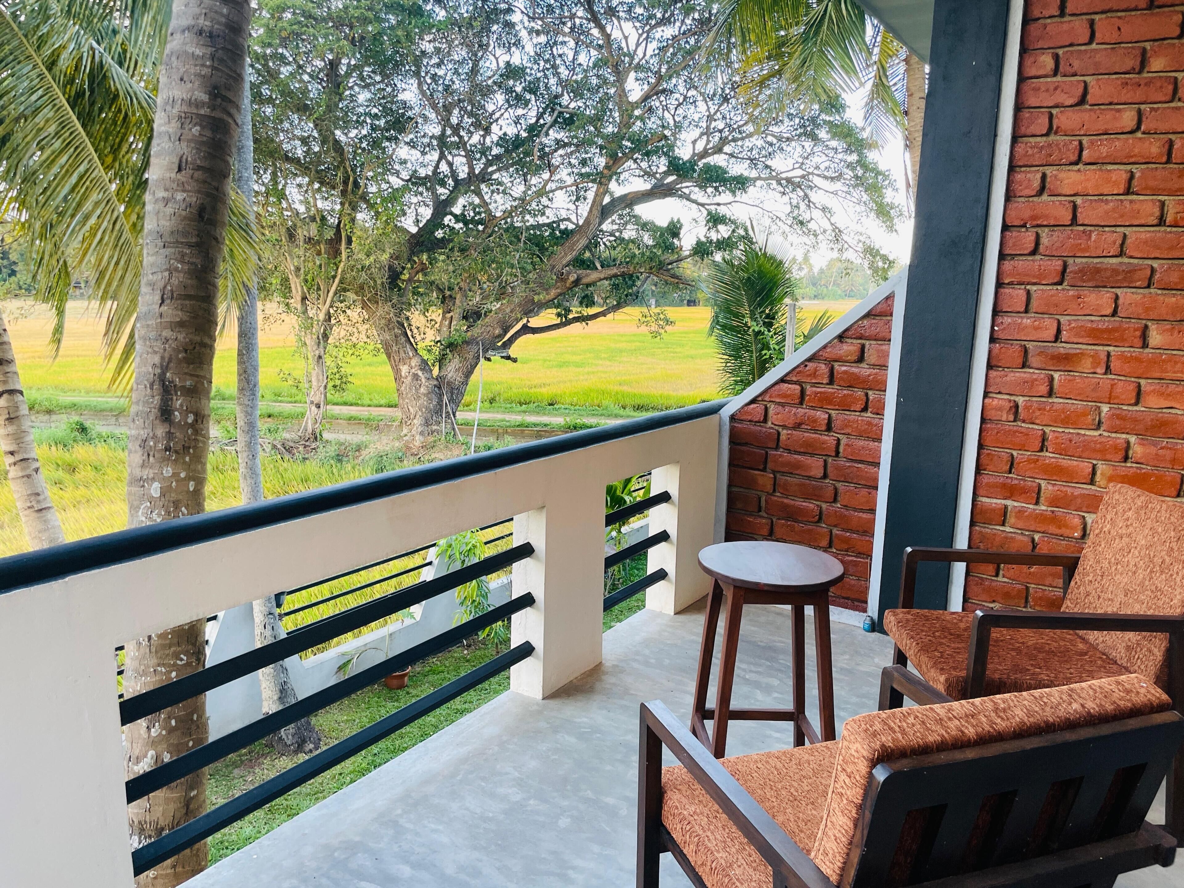 A balcony with a view of a green field, a brick wall, and a wooden chair.