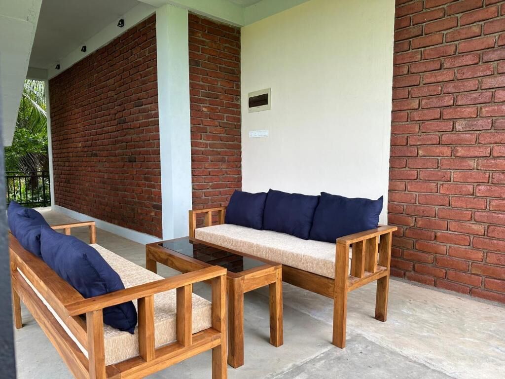 A patio area with wooden furniture, including a sofa and two chairs, against a brick wall.