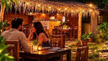 A couple dining at a rustic outdoor restaurant with wooden furniture and a thatched roof.