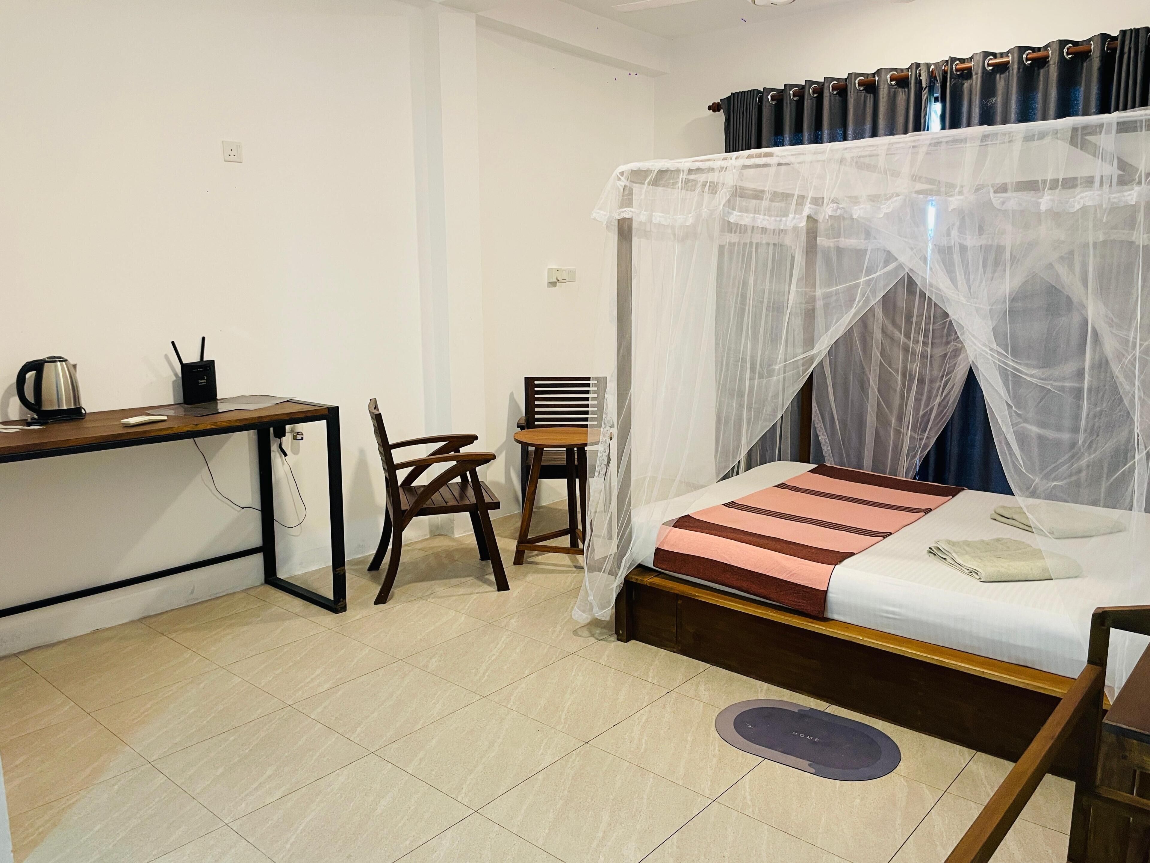 A bedroom with a bed, a desk, a chair, and a bedside table.