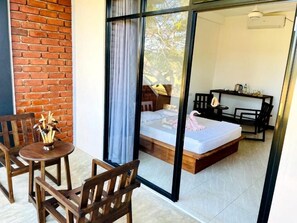 Habitación con cama, escritorio y silla. Se ve una ventana con cortinas, y una pared de ladrillo al exterior.