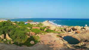 A coastal landscape with rocky terrain, greenery, and a beach with buildings in the distance. - Tranquil Sanctuary Yala (Tissamaharama)
