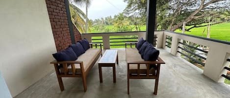 Un área de estar al aire libre con techo, con dos sofás de madera y una mesa, con vistas a un paisaje verde exuberante.
