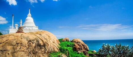 A white stupa on a rock with a clear blue sky and ocean in the background.