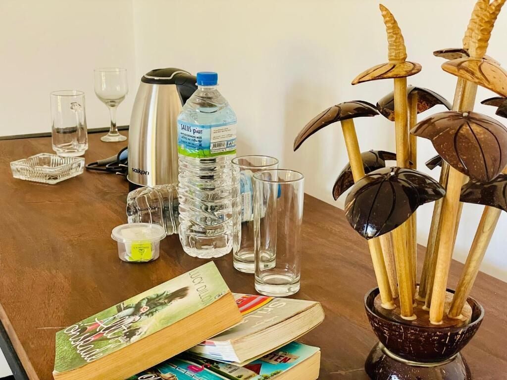 Une table en bois avec une bouteille d’eau, une bouilloire, des verres et une plante décorative.