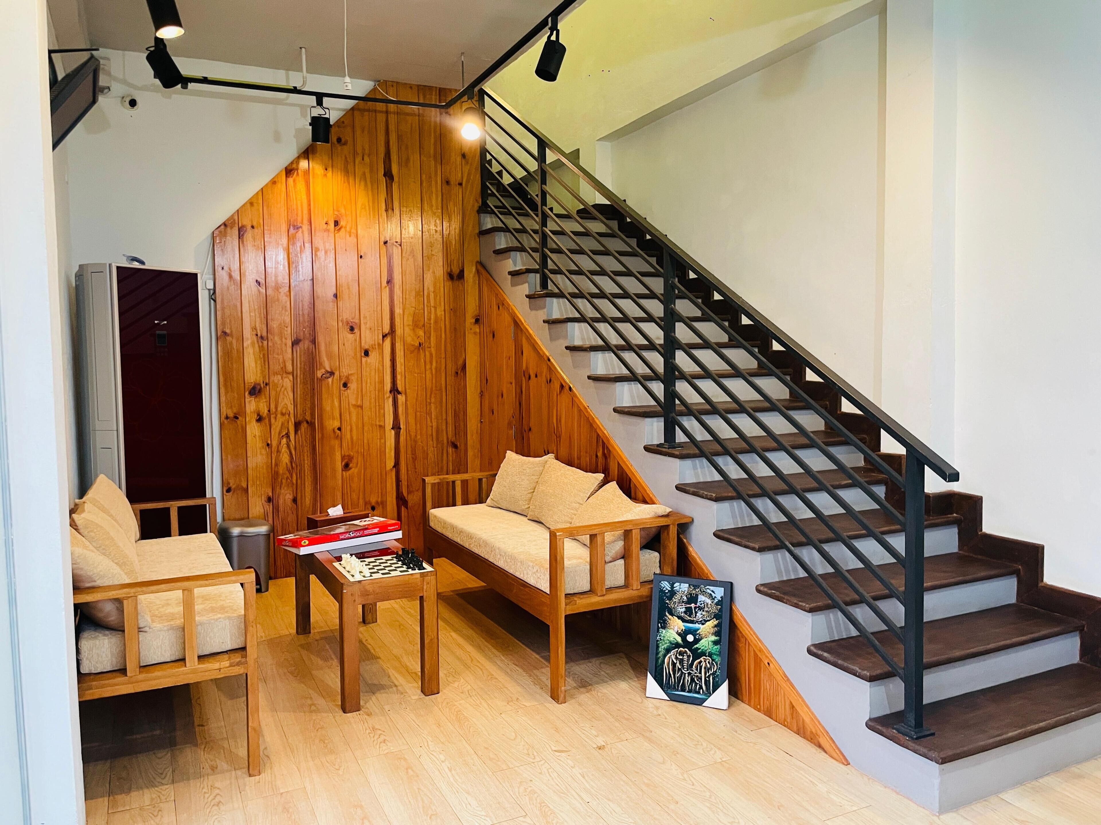 A modern living space with a wooden wall, a sofa, a coffee table with books, a chessboard, and a staircase.