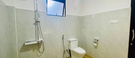 A small bathroom with a toilet, a shower, and a window.