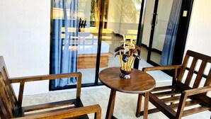 A room with a glass door leading to a balcony with a view of palm trees and a pool. There is a round wooden table with chairs and a decorative bowl on it. - Tranquil Sanctuary Yala (Tissamaharama)