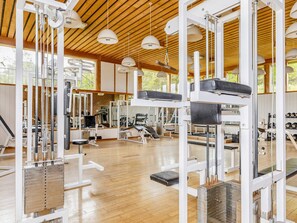 A gym with various exercise equipment, wooden flooring, and a high ceiling with hanging lights. - 1 Person Holiday Home on a Holiday Park in Hanstholm (Hanstholm)