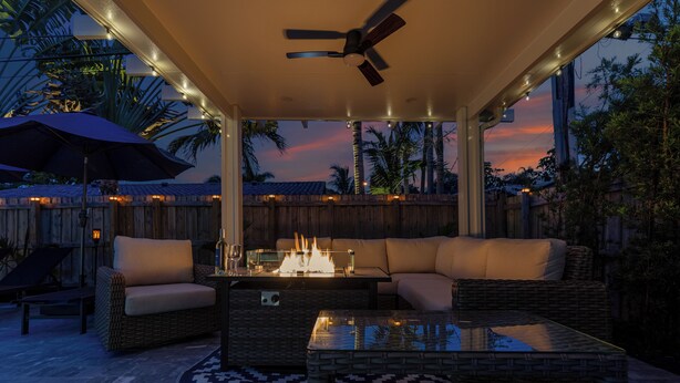 An outdoor patio with a glass-top table, wicker furniture, and a fire feature.