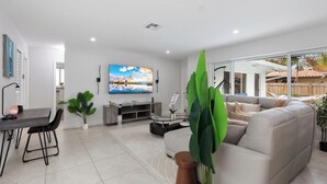 A modern living room with a white sofa, a dining table, and a TV.