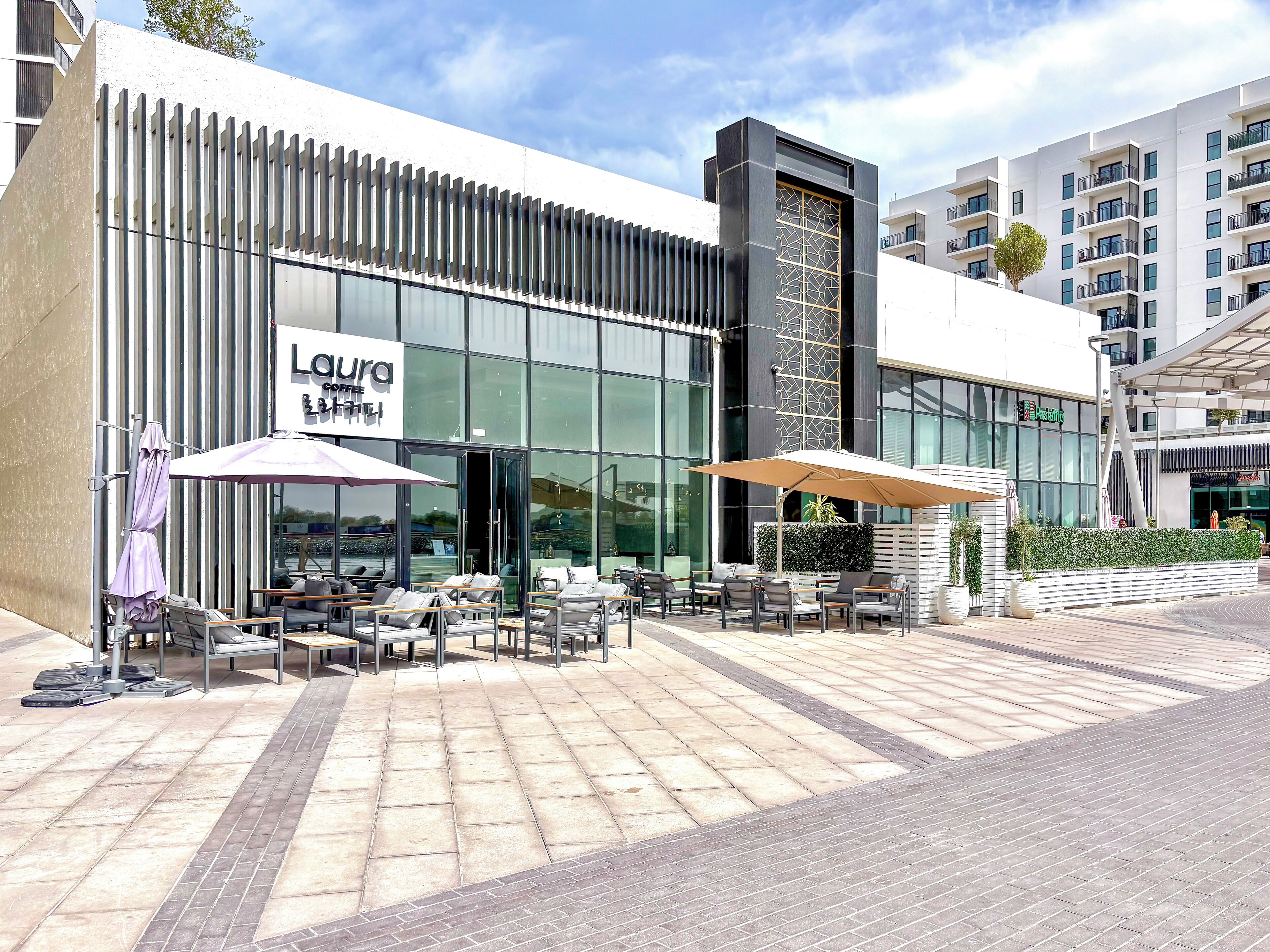 A modern building with a coffee shop named "Loura Coffee" and outdoor seating with umbrellas.