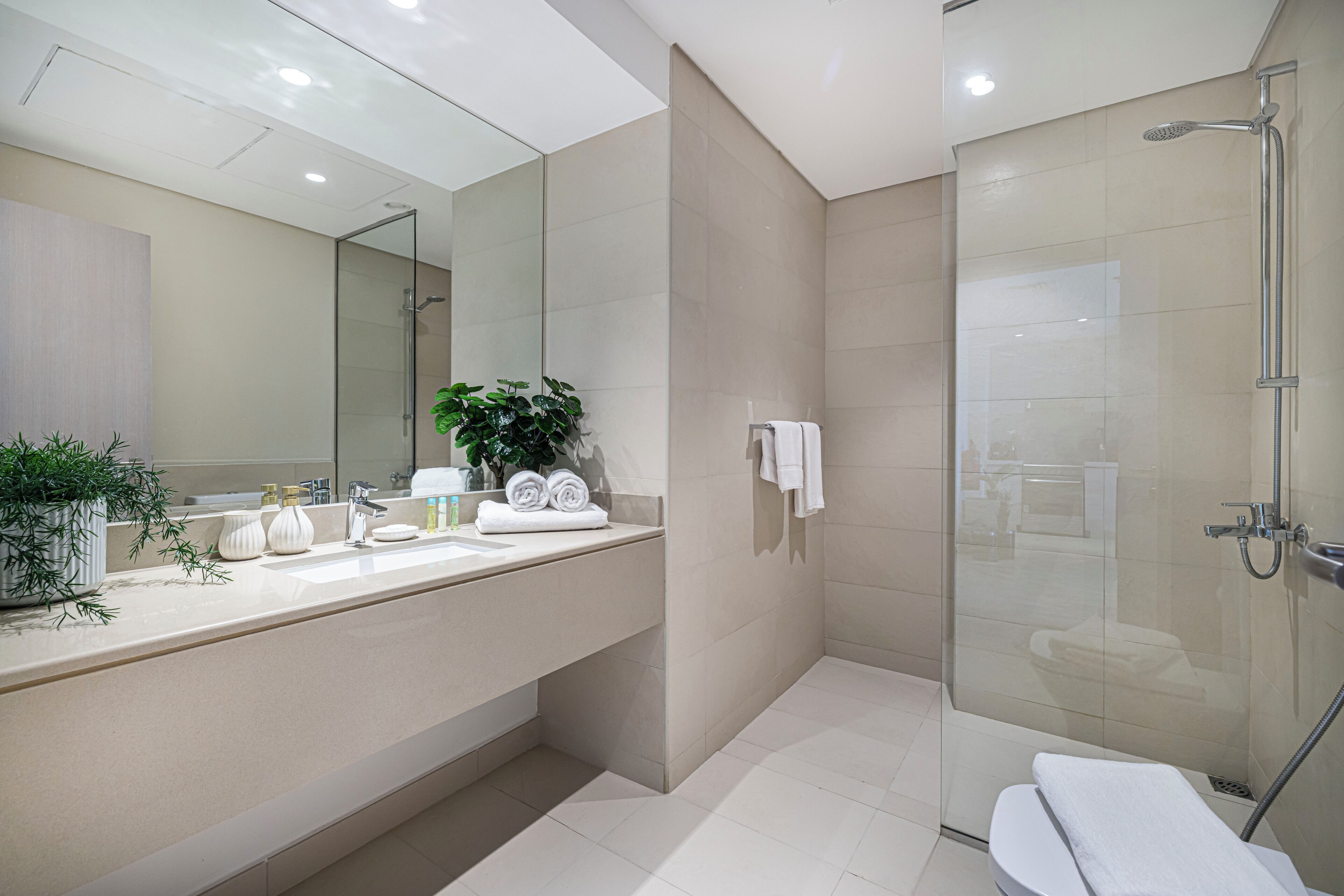 A modern bathroom with a glass-enclosed shower, a large mirror, and a vanity with toiletries.