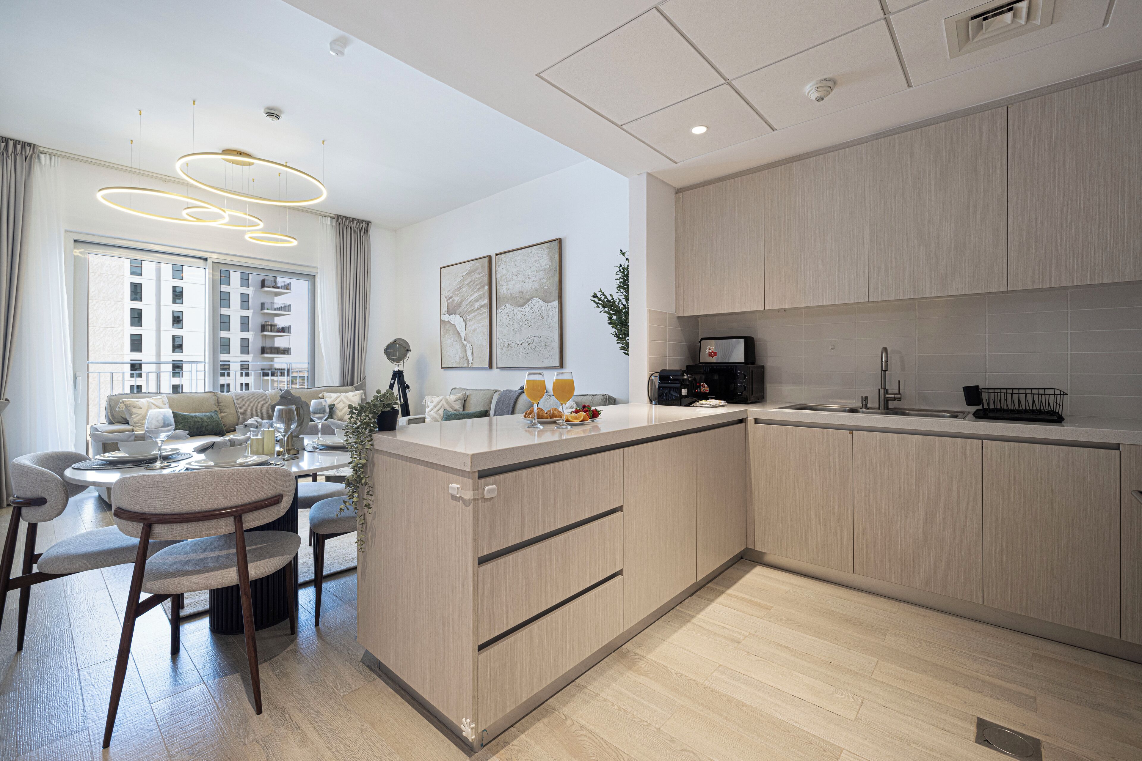 A modern kitchen with light wood cabinets, a central island, and a dining area with a round table and chairs.