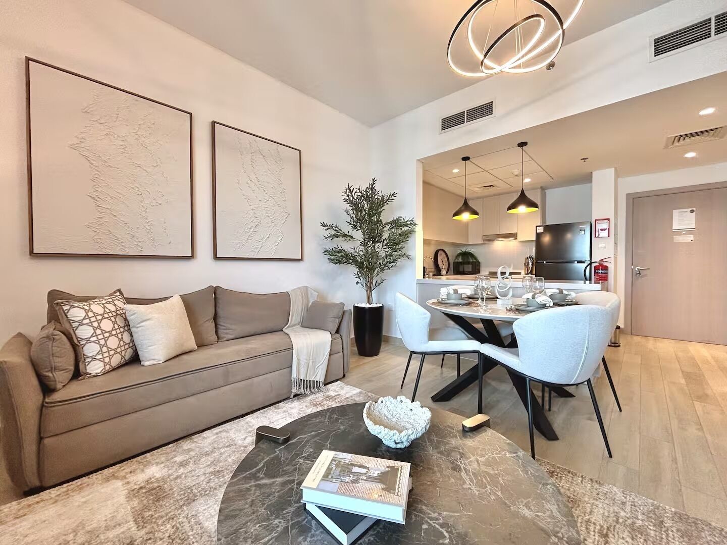 A modern living room with a sofa, coffee table, and artwork. There is a dining area with a table and chairs.