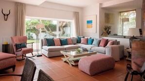 Ein Wohnzimmer mit einer Couch, Sesseln, einem Couchtisch und einem großen Fenster mit Vorhängen.