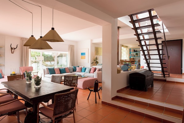 Un vaste espace de vie comprenant une table à manger, des chaises en osier, un canapé et un escalier.