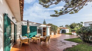 Eine Terrasse mit Fliesenboden, Gartenmöbeln und einem überdachten Bereich mit einer Schiebetür.