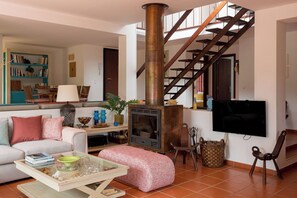 Un salon comprenant un canapé, une table basse, une cheminée, un téléviseur et un escalier.