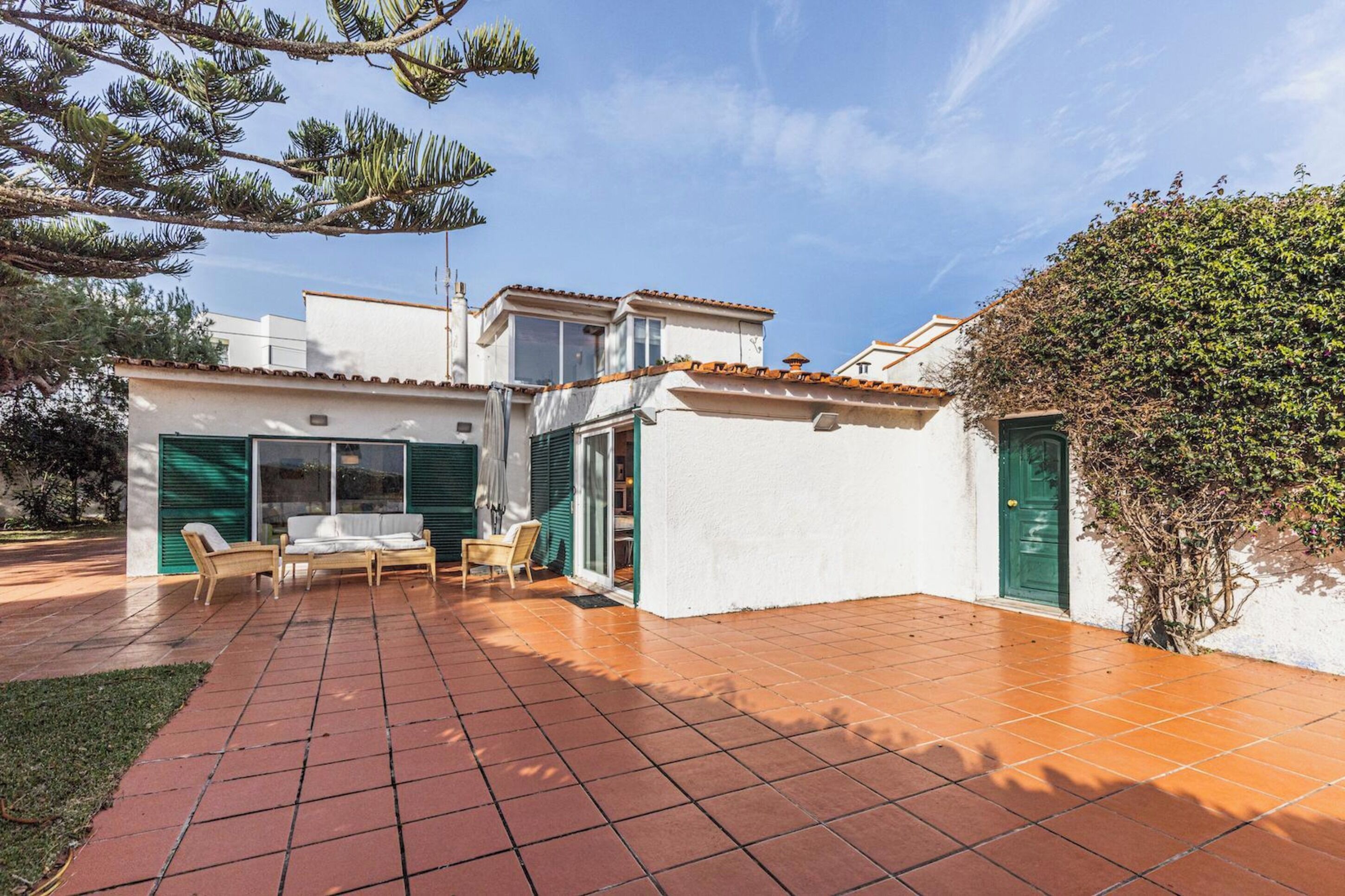 Une maison avec un patio carrelé, un coin repas avec des chaises et une porte verte.