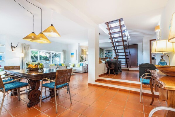 Amplia sala de estar con una mesa de comedor, sillas y una escalera que conduce a un nivel superior.
