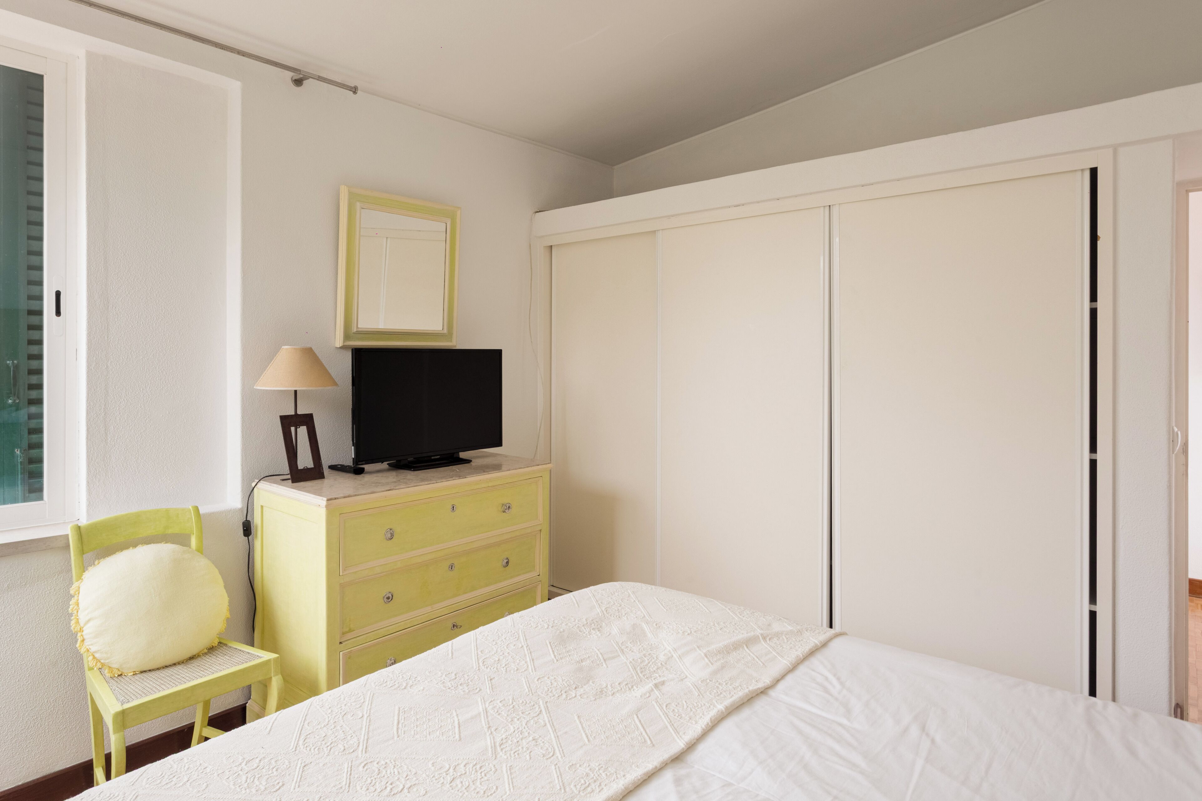 Un dormitorio con cama, cómoda, televisor, silla y armario.