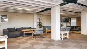 A spacious indoor area with a checkered carpet, multiple seating options including sofas and chairs, and a television mounted on the wall. - 4 Person Holiday Home on a Holiday Park in Fano (Fano)