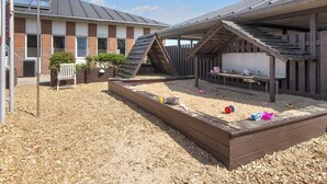 A backyard with a wooden play area, a brick building, and a metal roof structure. - 4 Person Holiday Home on a Holiday Park in Fano (Fano)