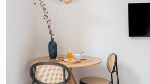 Un comedor con una mesa redonda, dos sillas, un jarrón con plantas secas, un vaso de jugo de naranja y un tazón con una cuchara.