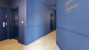 Un pasillo con paredes azules y suelo de madera, que conduce a puertas con números de habitación.