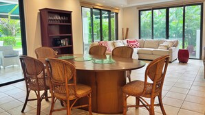 A dining area with a round table, wicker chairs, a bookshelf, and a sofa with cushions.