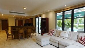 A spacious living room with a large sectional sofa, a dining area with a bar, and a view of a pool through large windows.