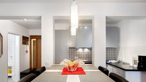 Une cuisine moderne dotée d’un îlot central, un coin repas avec une table et des chaises, et un couloir menant à une salle de bain.