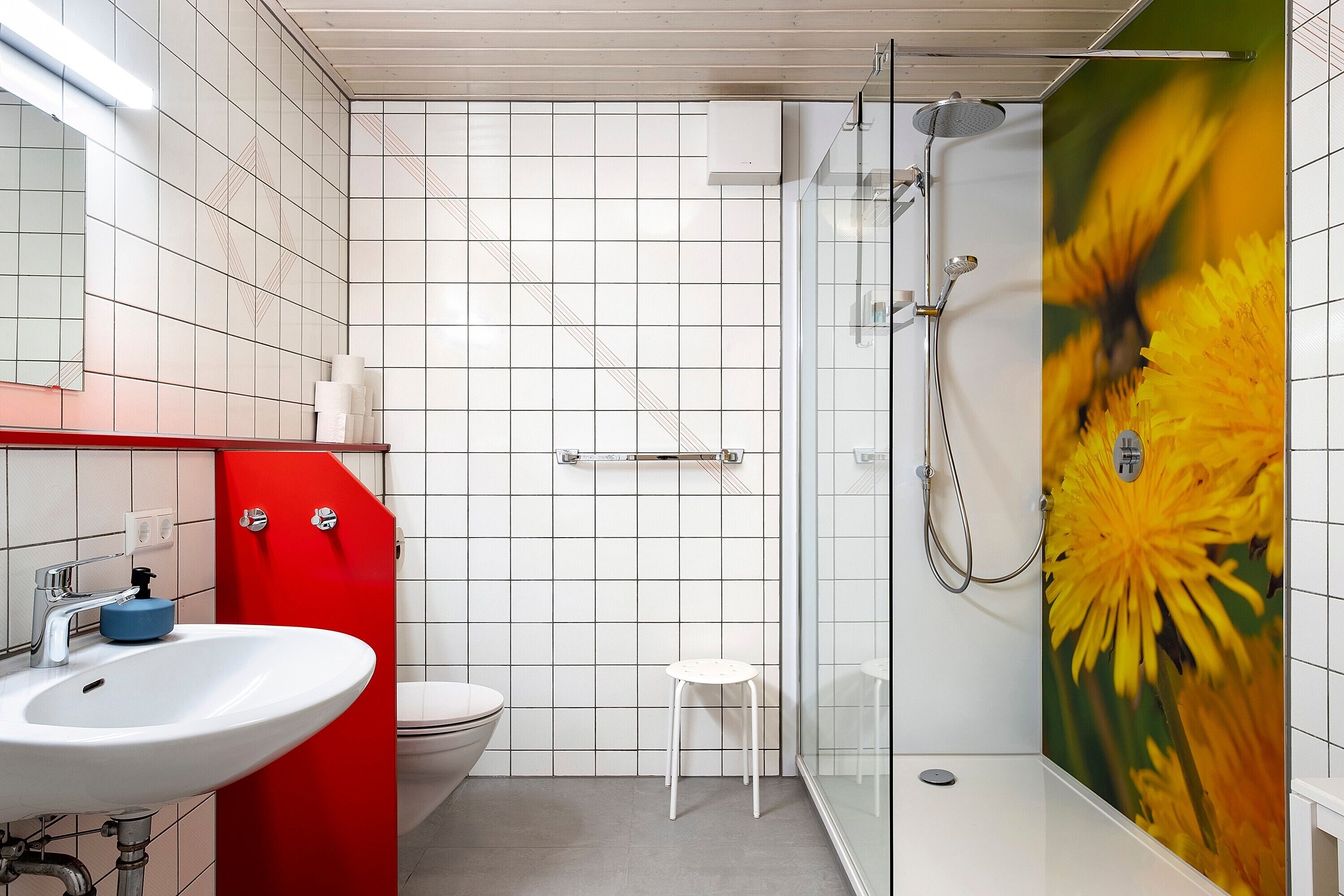 Un baño con lavamanos blanco, pared de acento roja, cabina de ducha de vidrio y un inodoro.