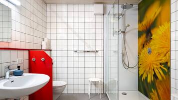 Un baño con lavamanos blanco, pared de acento roja, cabina de ducha de vidrio y un inodoro.