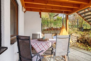 An outdoor patio with a table and chairs, a hanging light fixture, and a stone wall in the background.
