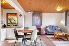 A modern living space with a wooden ceiling, a dining area with a round table and chairs, a sofa, and a small coffee table.