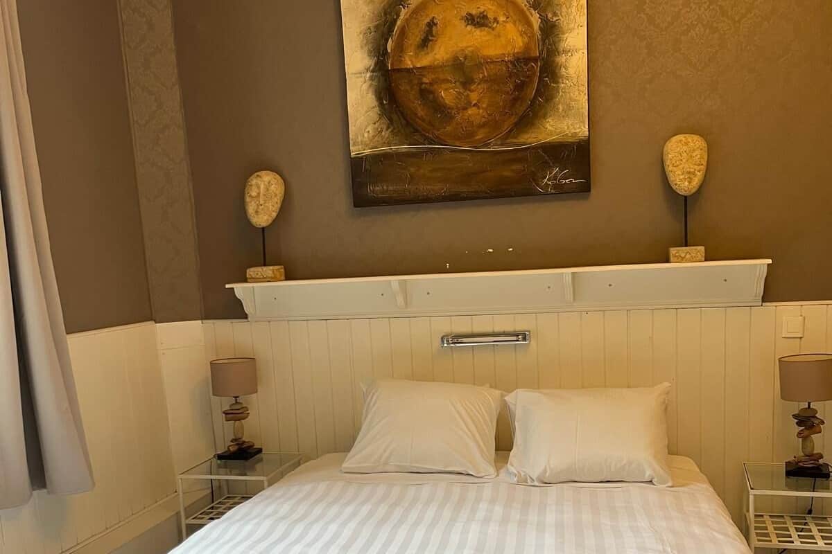 A bedroom with a large bed, two bedside tables, a nightstand, a wall-mounted painting, and a decorative stone sculpture.