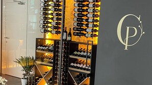 A wine cellar with multiple racks of wine bottles, a glass door, and a logo on the wall.