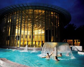 A modern building with a circular glass facade and a pool with water jets. - Hotel du Parc de 7 heures (Spa)