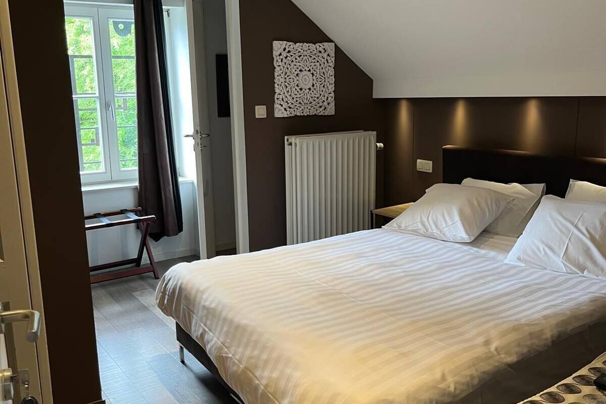 A bedroom with a bed, a radiator, a window with curtains, and a door.