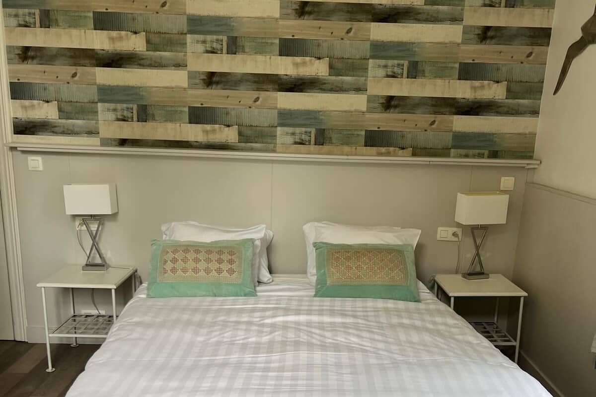 A double bed with a quilted headboard, two bedside tables with lamps, and a wall with a wooden plank pattern.