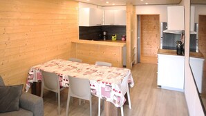 Eine kompakte Küche mit Holzwänden, ein Essbereich mit Tisch für vier Personen und ein kleiner Kühlschrank.
