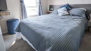Un dormitorio ordenado con cama, un escritorio pequeño, una silla y una ventana con cortinas.