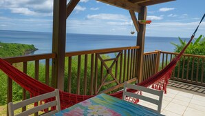 A wooden deck with a hammock and a table, overlooking a coastal view. - Sea view bungalow (Bouillante)